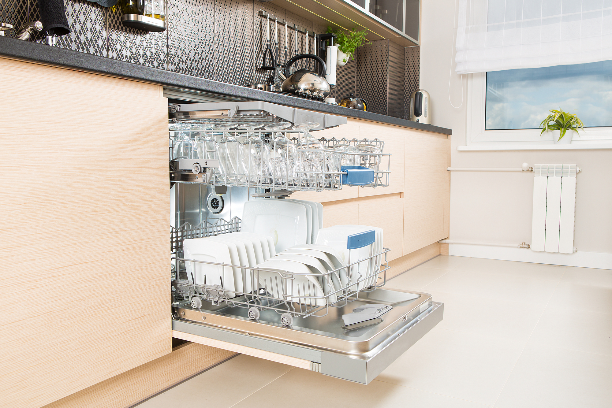 Open dishwasher in a modern kitchen, showcasing clean glasses and plates. The sleek design emphasizes an efficient, stylish home environment.