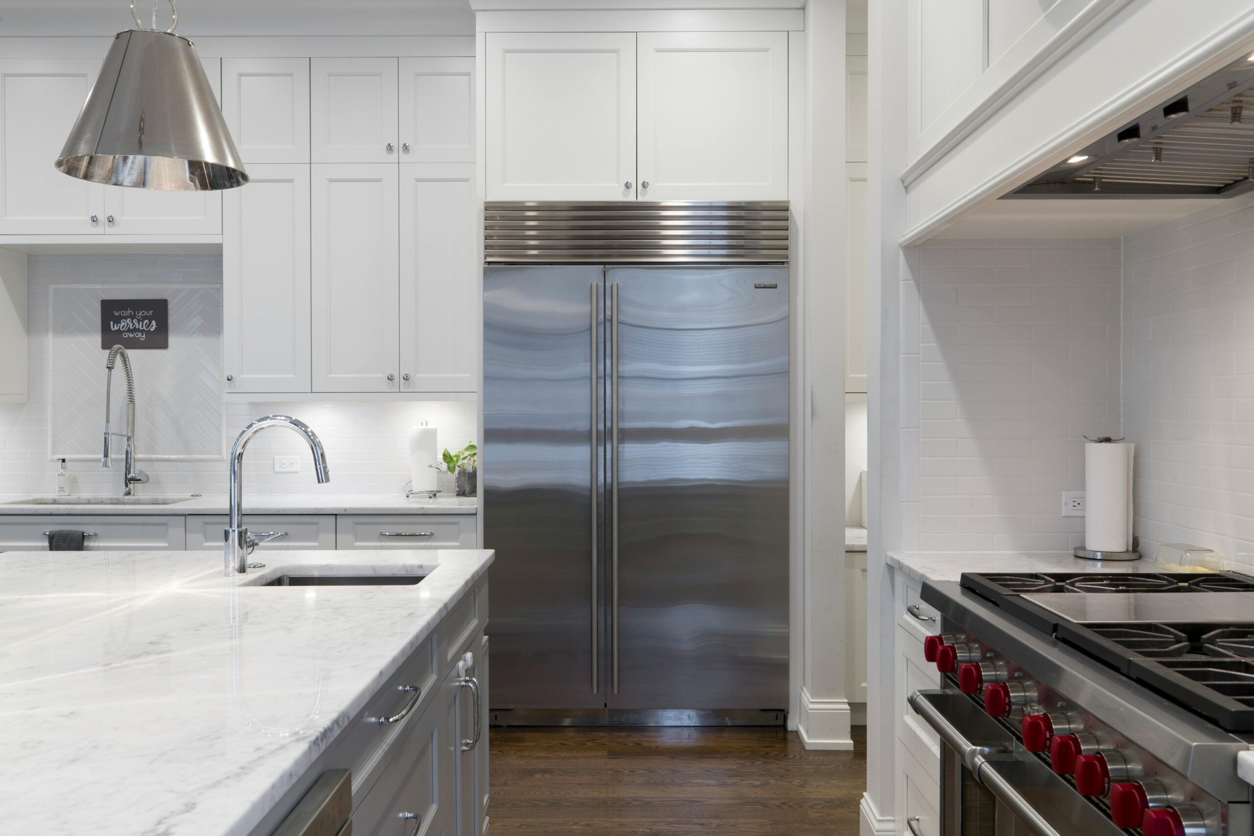 Modern kitchen featuring stainless steel refrigerator, marble countertops, and a professional stove. Illuminated space with minimalist design elements.