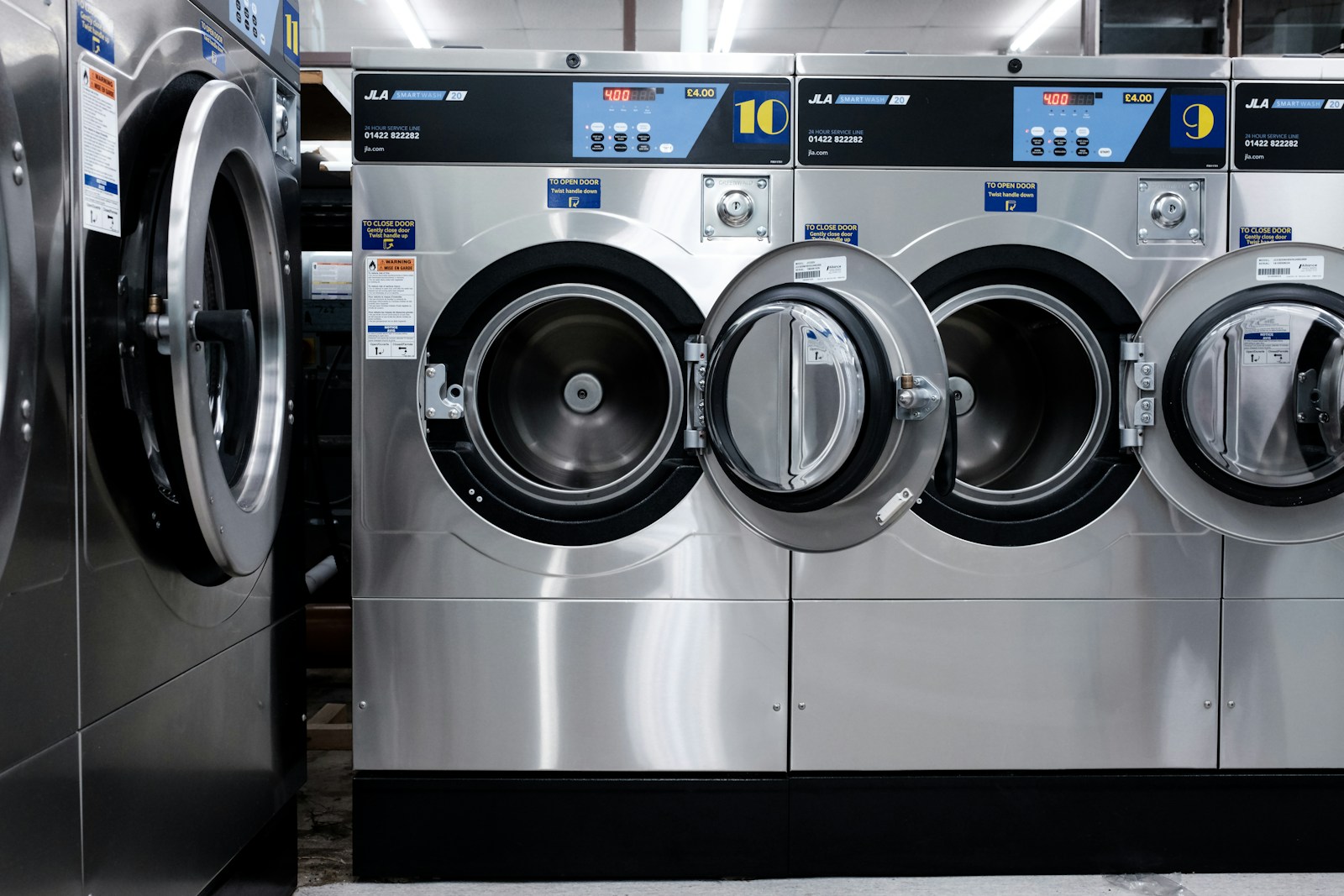 Three industrial washing machines lined up in a laundromat, showcasing their digital displays and stainless steel exteriors.