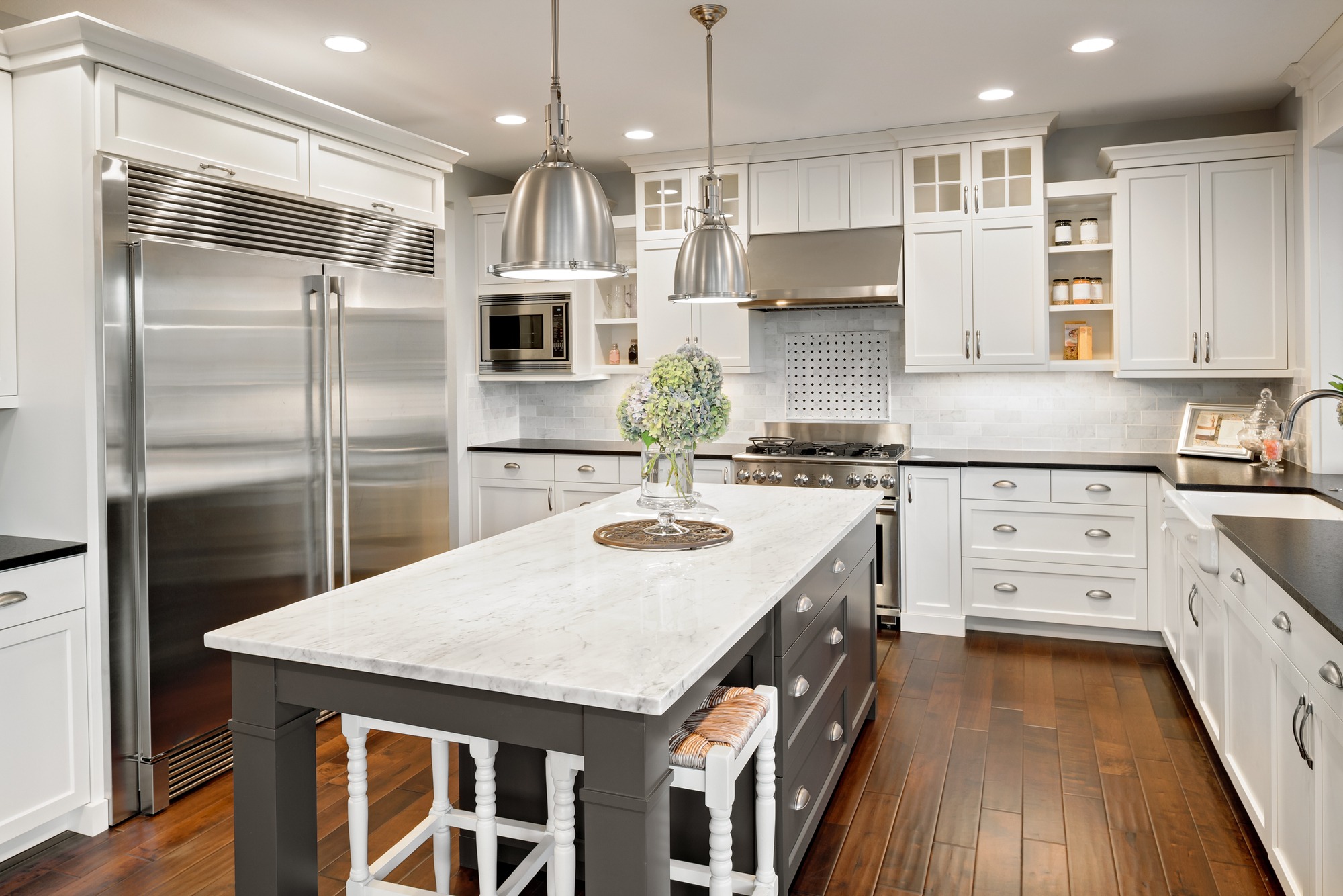 Modern kitchen featuring sleek stainless steel appliances, white cabinetry, and a large marble island with a floral centerpiece, emphasizing contemporary design.